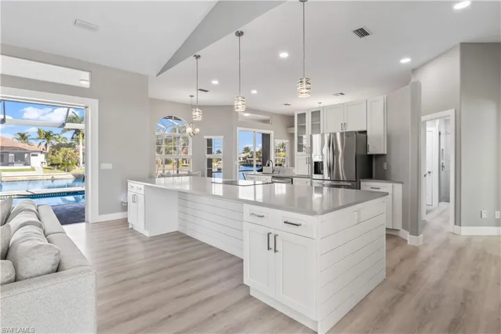 Kitchen with white cabinetry, glass insert cabinets, pendant lighting, open floor plan, and stainless steel refrigerator with ice dispenser