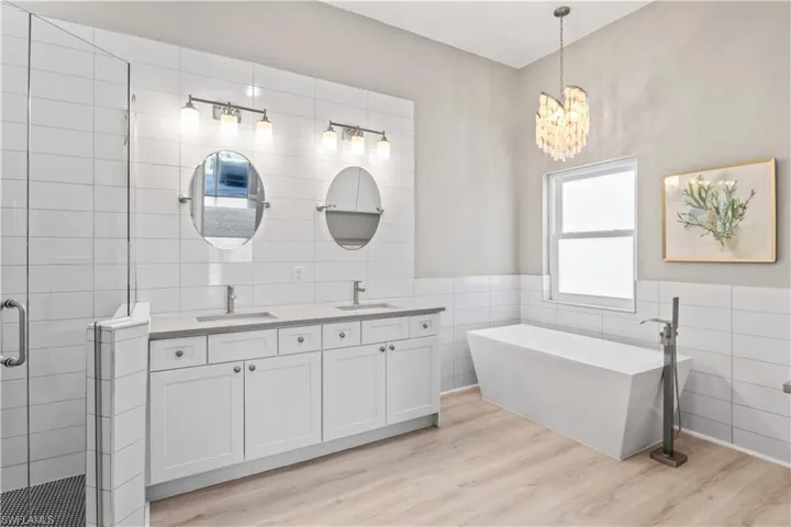Bathroom with tile walls, double vanity, wainscoting, a stall shower, and a freestanding bath