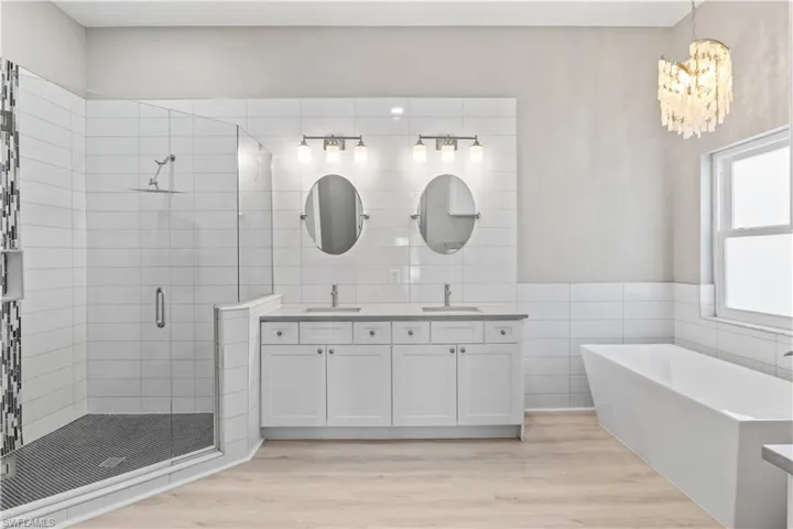 Full bathroom with tile walls, double vanity, a shower stall, a freestanding bath, and light wood finished floors