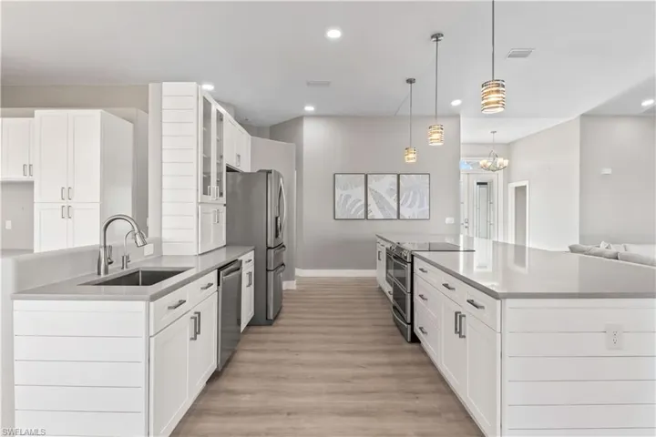 Kitchen with white cabinetry, appliances with stainless steel finishes, glass insert cabinets, decorative light fixtures, and light wood-type flooring