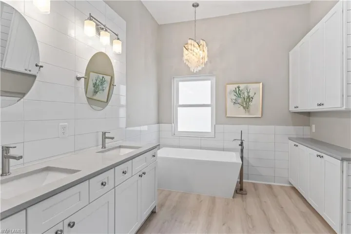 Bathroom featuring tile walls, a soaking tub, double vanity, light wood-style flooring, and a wainscoted wall