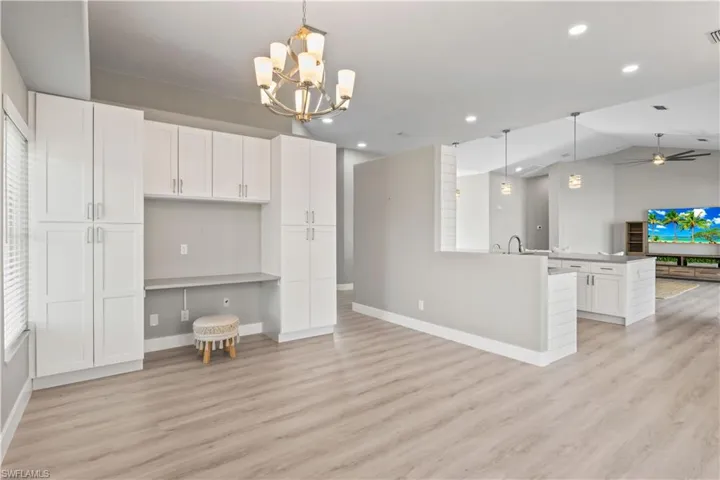 Kitchen with hanging light fixtures, open floor plan, white cabinetry, lofted ceiling, and a chandelier
