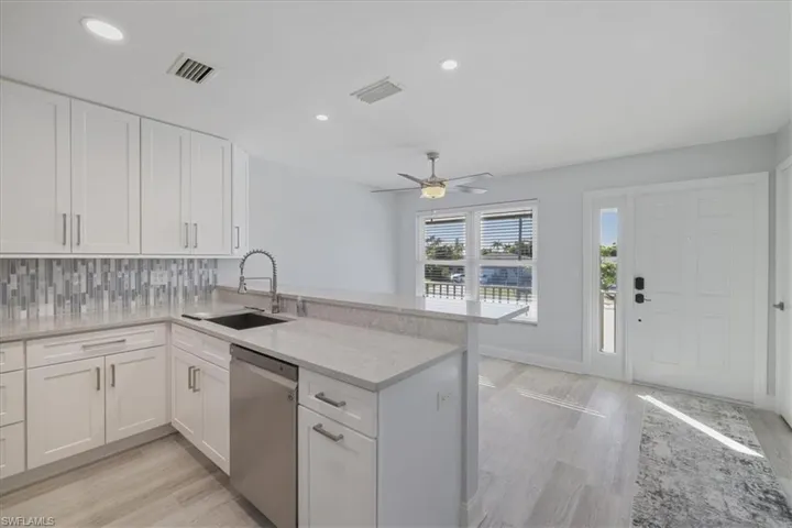 Kitchen with white cabinetry, light stone countertops, stainless steel dishwasher, backsplash, and a peninsula