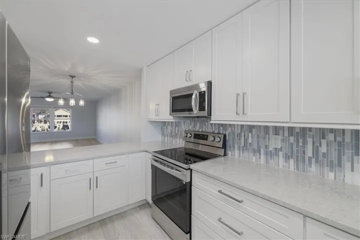 Kitchen with stainless steel appliances, white cabinets, light stone counters, and decorative backsplash