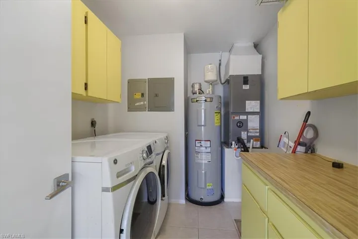 Laundry room with cabinet space, electric water heater, washing machine and clothes dryer, electric panel, and light tile patterned floors