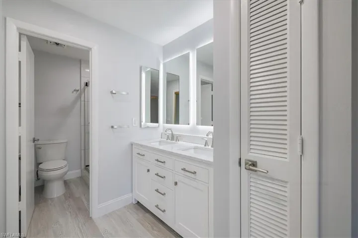 Full bath with a closet, double vanity, a stall shower, and light wood-type flooring