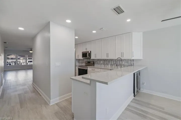Kitchen featuring ceiling fan, white cabinetry, stainless steel appliances, light stone counters, and light wood-style flooring