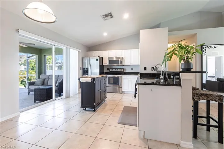 Kitchen featuring stainless steel appliances, lofted ceiling, a kitchen breakfast bar, white cabinets, and a peninsula