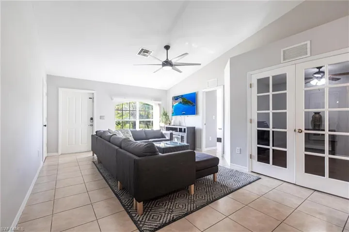 Living room with a ceiling fan, vaulted ceiling, tile patterned floors, and french doors