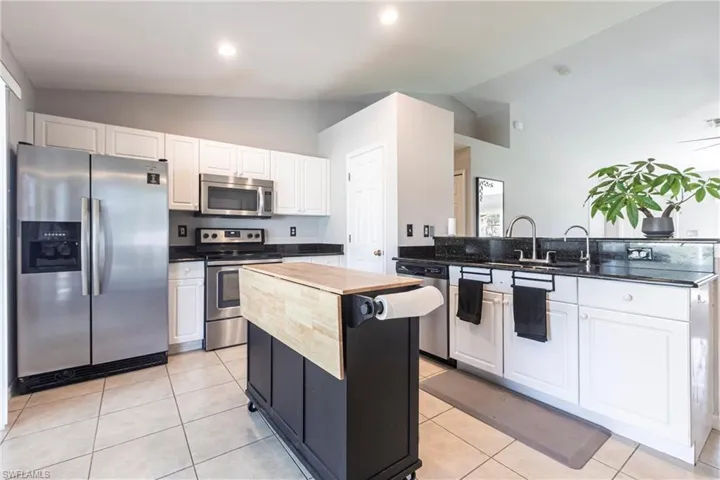 Kitchen with appliances with stainless steel finishes, vaulted ceiling, a peninsula, white cabinets, and a center island