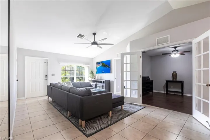 Living room with a ceiling fan, vaulted ceiling, light tile patterned floors, and french doors