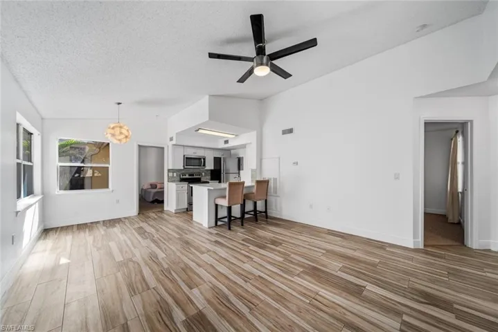 Unfurnished living room featuring ceiling fan with notable chandelier, light hardwood / wood-style floors, a textured ceiling, and vaulted ceiling