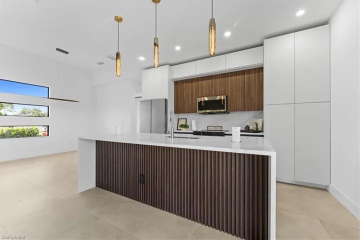 Kitchen featuring appliances with stainless steel finishes, modern cabinets, light countertops, a sink, and a kitchen island with sink