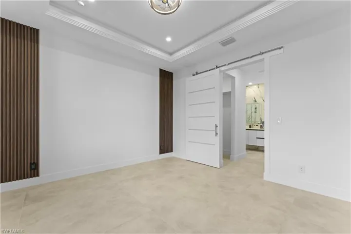Primary room with ornamental molding, a tray ceiling, a barn door, baseboards, and recessed lighting