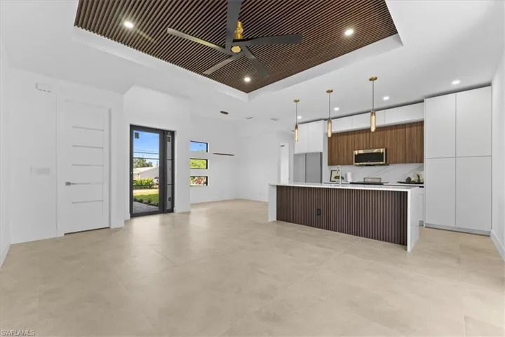 Kitchen featuring a tray ceiling, stainless steel microwave, modern cabinets, a ceiling fan, and light countertops