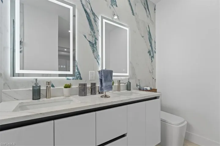 Full bath featuring double vanity, toilet, and baseboards
