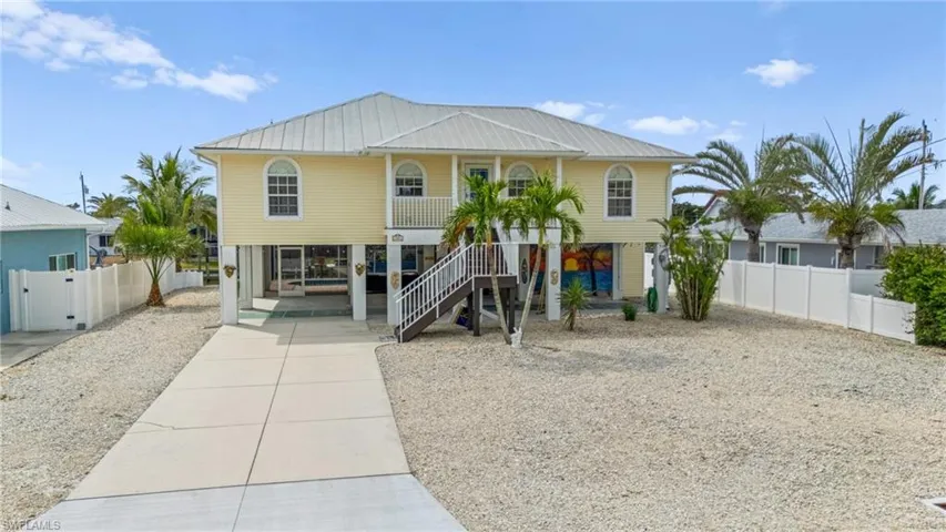 Coastal home featuring covered porch, stairway, driveway, metal roof, and a carport-Virtually enhanced