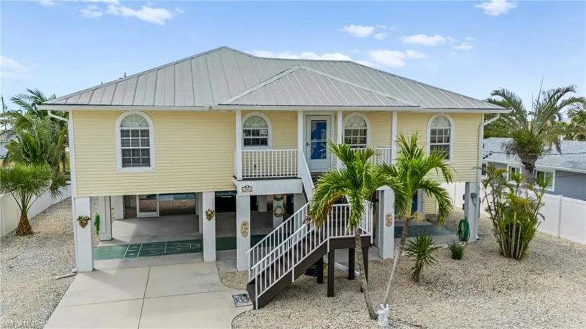 Coastal home featuring covered porch, stairway, driveway, metal roof, and a carport -Virtually enhanced