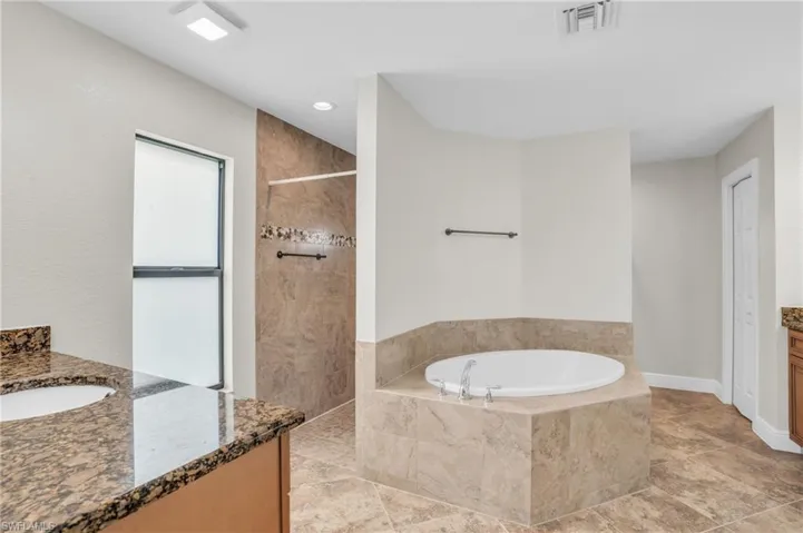 Bathroom with tile floors, a relaxing tiled bath, and vanity