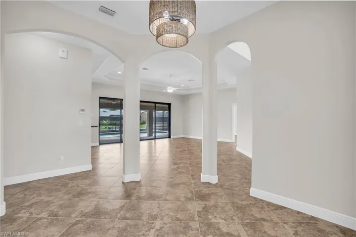 Tiled empty room featuring ceiling fan with notable chandelier and a tray ceiling