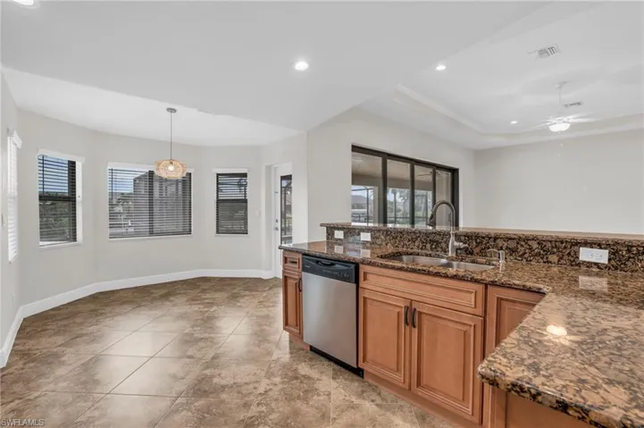 Kitchen with dishwasher, sink, ceiling fan, light tile floors, and a raised ceiling