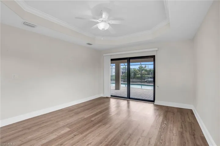 Empty room with ceiling fan, a tray ceiling, crown molding, and hardwood / wood-style flooring