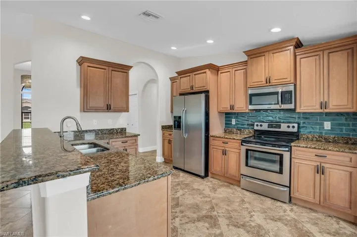 Kitchen with appliances with stainless steel finishes, dark stone counters, kitchen peninsula, sink, and light tile floors