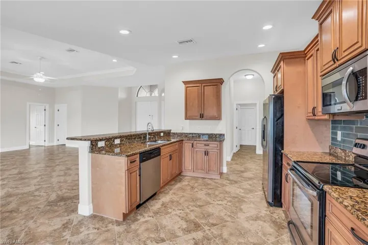 Kitchen with stainless steel appliances, dark stone counters, kitchen peninsula, ceiling fan, and light tile floors