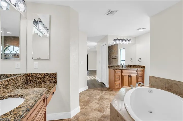 Bathroom featuring a relaxing tiled bath, double sink vanity, and tile floors