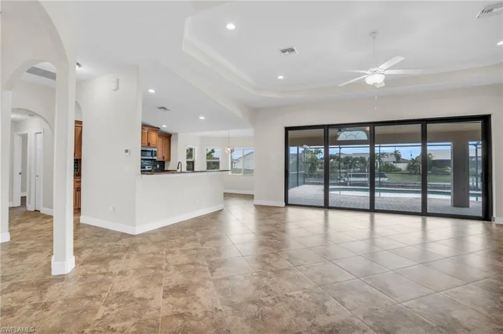 Unfurnished living room with a raised ceiling, ceiling fan, and light tile floors