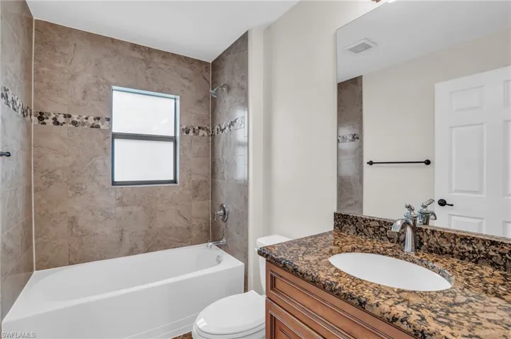 Full bathroom with tiled shower / bath combo, toilet, and vanity with extensive cabinet space