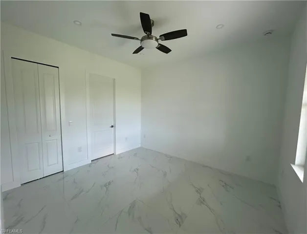 Primary bedroom with a closet and bathroom featuring marble flooring, baseboards, and a ceiling fan