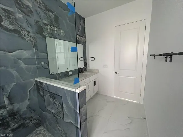 Primary bathroom with marble tiles, double vanity, and a shower