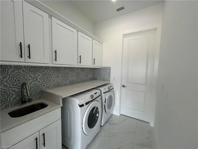 Laundry with sink, cabinet space, washing machine and dryer, light marble countertops, and decorative backsplash