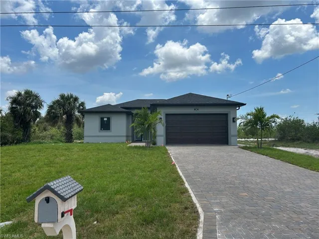 View of front of house with stucco siding, a front yard, decorative driveway, and a garage