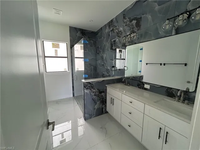 Primary bathroom with marble floors, a marble finish shower, and a double vanity