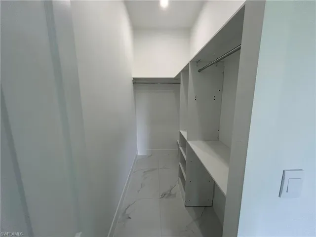 Spacious closet in primary bedroom featuring cabinetry and light marble finish flooring