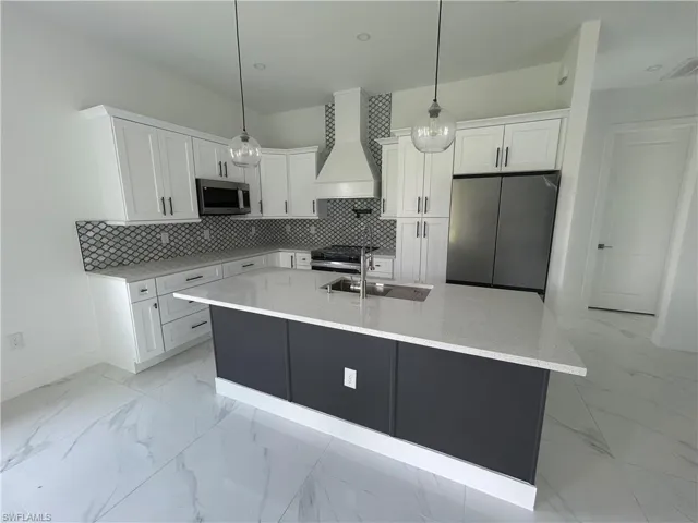 Kitchen with exhaust hood, stainless steel appliances, backsplash, and pendant lights