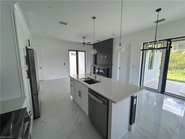 Kitchen with stainless steel appliances, a sink, light marble finish floors, white cabinetry, and a center island with sink