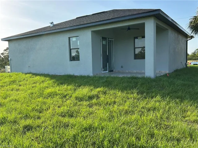 Rear view of house with a yard, stucco siding, a ceiling fan, and roof with shingles