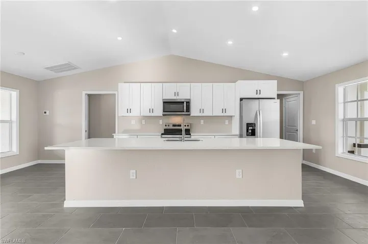 Kitchen with plenty of natural light, stainless steel appliances, a kitchen island with sink, white cabinetry, and recessed lighting