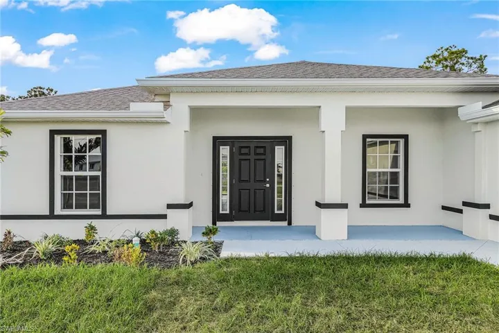 Doorway to property featuring stucco siding, a lawn, and a shingled roof
