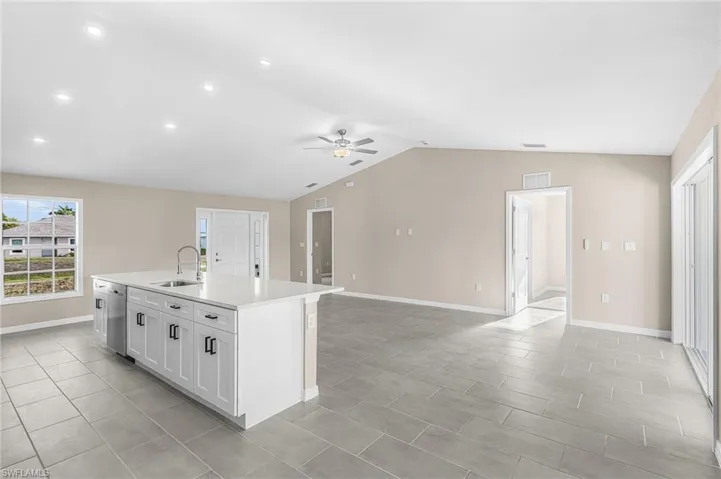 Kitchen with ceiling fan, a center island with sink, white cabinetry, open floor plan, and light stone countertops