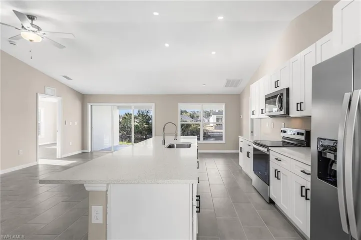 Kitchen with lofted ceiling, stainless steel appliances, white cabinets, a large island, and a ceiling fan