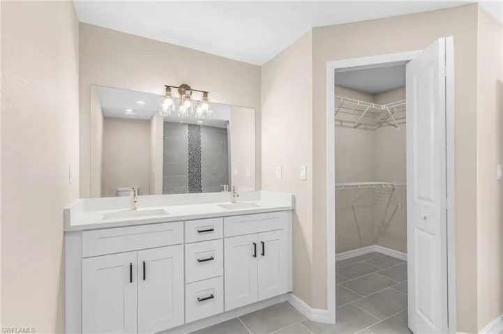 Bathroom featuring double vanity, light tile patterned floors, a walk in closet, and a tile shower