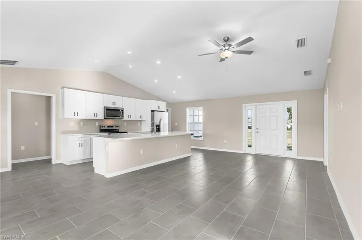Kitchen featuring white cabinetry, a center island with sink, ceiling fan, stainless steel appliances, and open floor plan