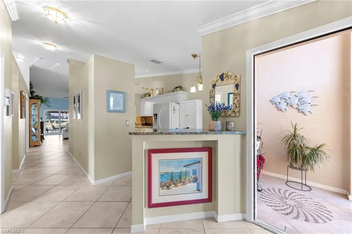 Kitchen featuring hanging light fixtures, dark stone countertops, crown molding, stainless steel fridge with ice dispenser, and light tile patterned flooring