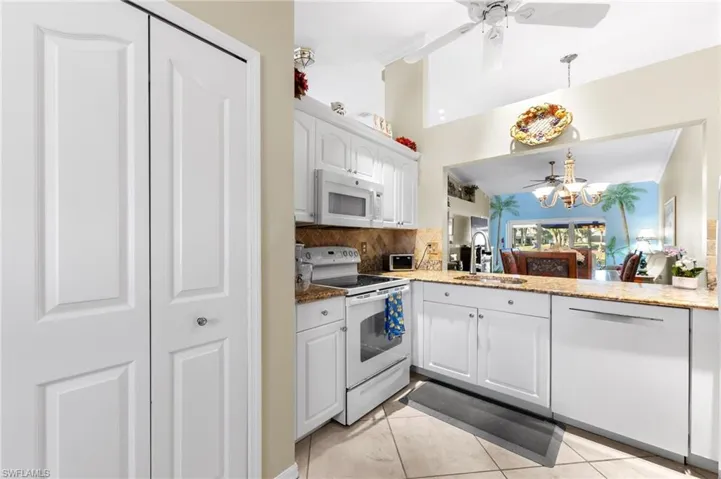 Kitchen with a ceiling fan, white appliances, white cabinets, dark stone counters, and decorative backsplash