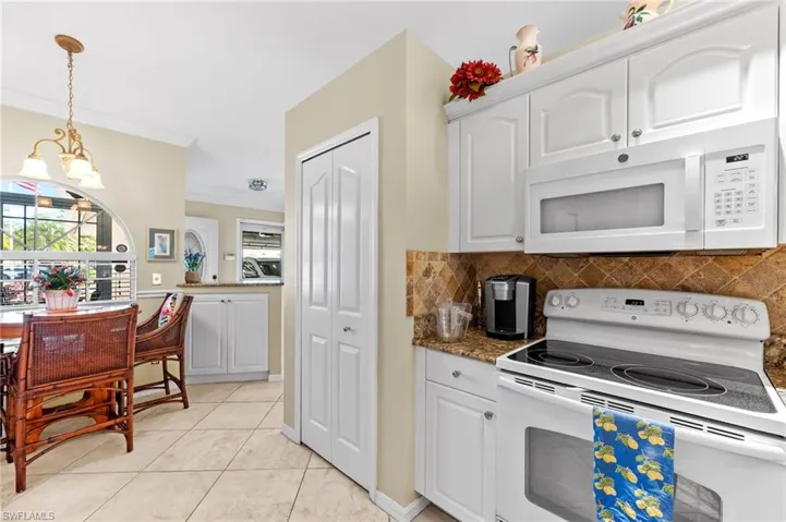 Kitchen with white appliances, white cabinets, ornamental molding, a chandelier, and dark stone countertops