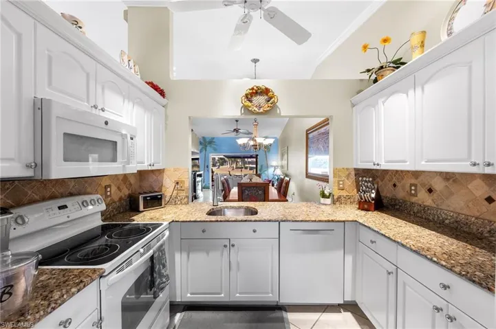 Kitchen featuring white appliances, ceiling fan, and dark stone counters
